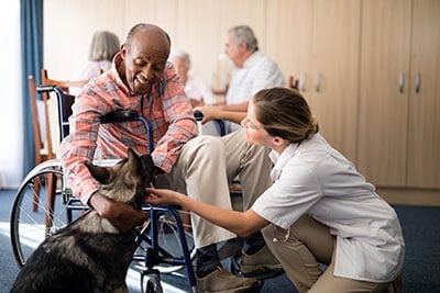 Elderly patient and medical assistant petting a dog